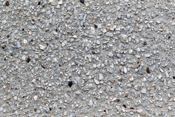 Concrete wall with decorative coating of small pebbles of different sizes. The surface is rough. Pebbles of different colors, gray, white, black and beige and of different shapes.