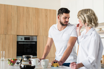 young woman feeding handsome boyfriend at morning in kitchen
