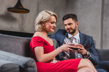 beautiful fashionable couple in suit and red dress drinking wine together