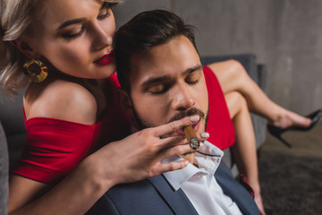 close-up view of sexy girl in red dress holding cigar while boyfriend smoking it