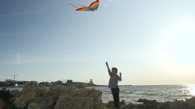 children's sports games. silhouette little kid boy control flying colorful kites. seascape sky clouds sun summer vacation