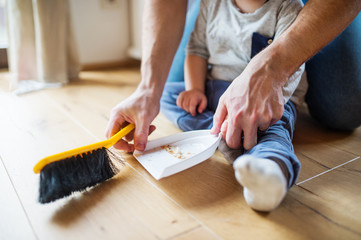 Unrecognizable father and toddler with brush and dustpan.