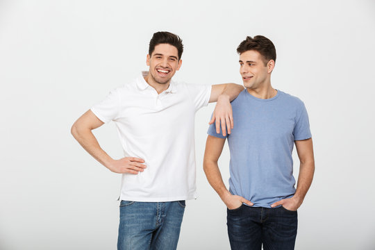Two handsome men fellas 30s wearing casual t-shirt and jeans smiling and posing together on camera, isolated over white background