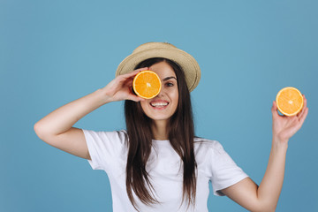 Brunette girl in yellow skirt holds oranges before her eyes and smiles posing in the studio