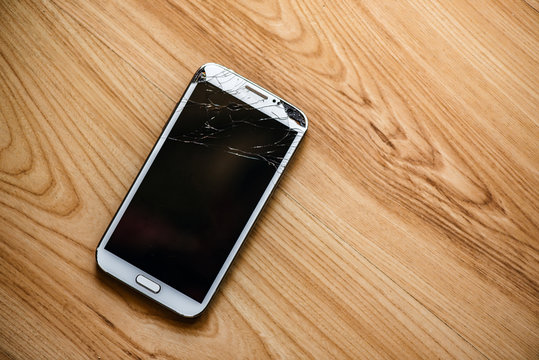 Phone with a broken screen on a wooden background.