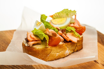 Sandwich with Vegetables and Smoked Salmon on Wooden Plate Isolated on White Background. Salmon, eggs, lettuce and tomatoes on Bread, top view