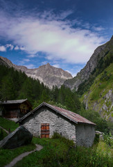 beautiful lush mountain valley with old cottages and high alpine peaks behind