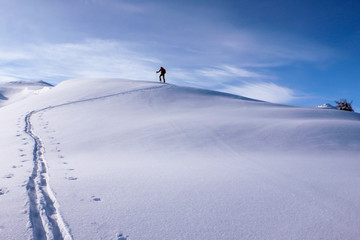 a backcountry skier hiking along a mountain ridge towards the summit near Klosters in the Swiss Alps in deep winter