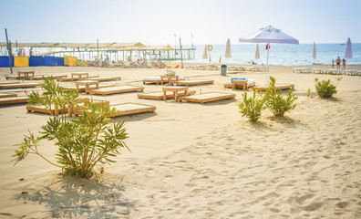 Obraz premium Sandy beach on blue sea background. Umbrellas and deck chairs on shore of sea. Summer day on beach rest. Vacation concept. View on sea beach in sunny clear day in Turkey Konakli.