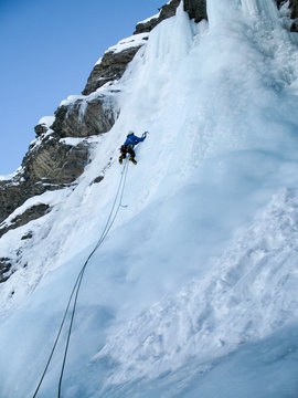 male ice climber in a blue jacket on a steep ice fall in winter