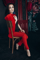 Attractive brunette in red suit sits on the old chair in dark studio