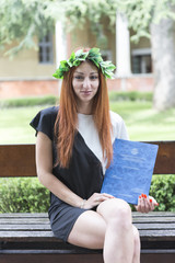 Portrait of a beautiful redhead girl holding her university final exam with a laurel wreath on her...