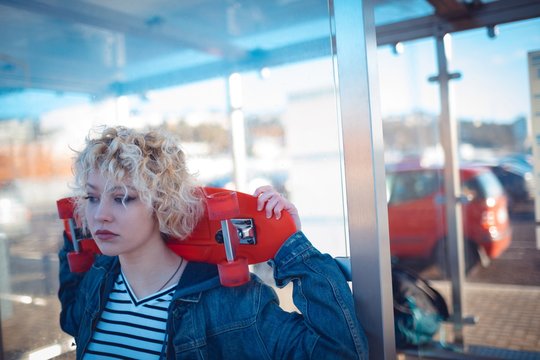 Woman holding skateboard at bus stop