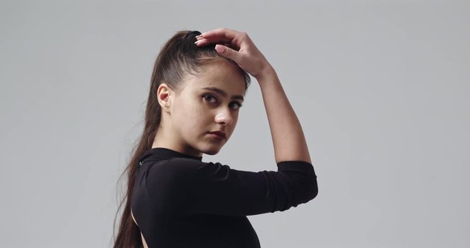 The young beautiful ballerina dancing on a studio white background wearing black leotard and ponytail. Slow motion.