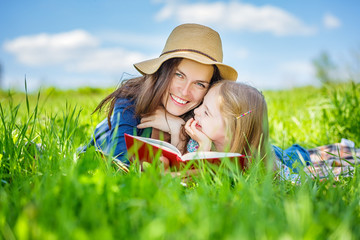 Mother and daughter lying on green grass enjoy reading book