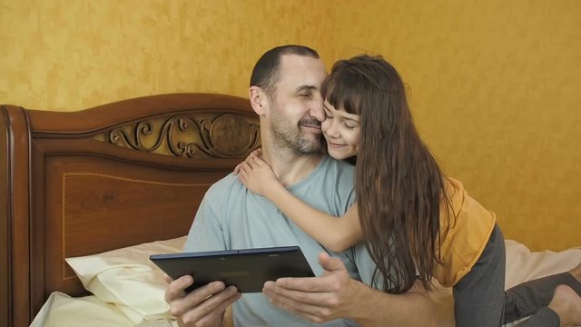 The daughter hugs her father. Dad with a tablet.