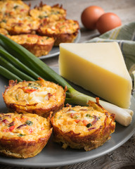 Muffins with scrambled eggs, cheese, bacon, potato and red pepper. Breakfast concept. Gray, rustic wooden background.