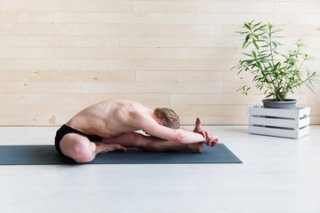 Sporty man doing Paschimottasana pose on yoga class