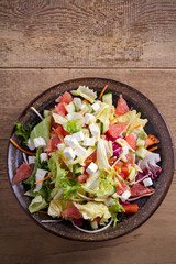Healthy vegetarian food: citrus grapefruit, tomato, lettuce and cucumber salad with feta cheese in bowl on wooden table. overhead, vertical