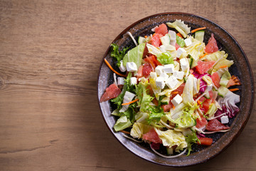 Healthy vegetarian food: citrus grapefruit, tomato, lettuce and cucumber salad with feta cheese in bowl on wooden table. overhead, horizontal