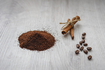 Coffee beans, ground powder and cinnamon sticks on a wooden background