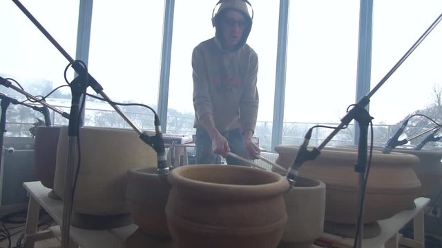 The drummer in a sweatshirt and glasses plays with drumsticks on clay pots