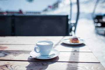 Cup of coffee with saucer on wooden outdoor table in wintersport area.