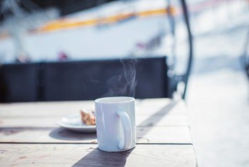 Steamy cup of coffee on wooden outdoor table in wintersport area.