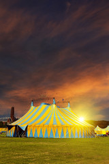 Unamed circus tent under a warn sunset and chaotic sky without the name of the circus company which...