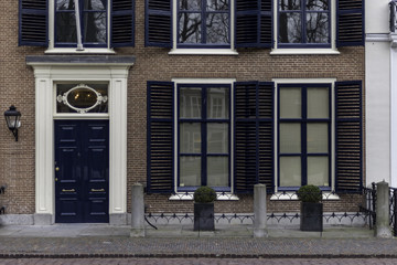 Victorian style wooden front door and windows along a main road and protected by concrete poles and flowers pots against car parking