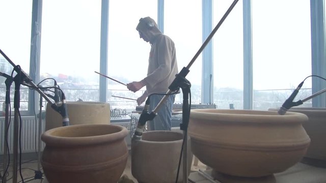 A man in a sweatshirt plays concept music on clay pots