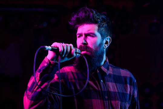 Man with enthusiastic face holds microphone, singing song, black background.