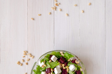 Obraz na płótnie Canvas Salad of Beetroot, Feta cheese and lettuce leaves with pine nuts on white wooden background. Empty space