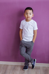 the child is standing in a white T-shirt on a lilac background. Mock up.