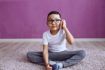 Fototapeta premium A little boy is sitting on the floor with a phone. Mock up