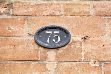 House number 75 sign fixed to brick wall