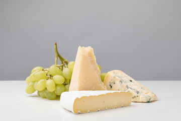 Closeup view of three types of cheese and grapes on gray