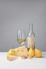 Cheddar and maasdam cheese, pears, almond, wine glass and bottle on gray