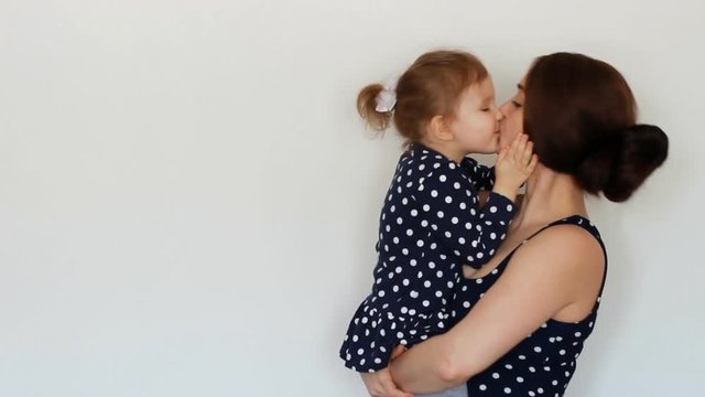 A happy mother holds a daughter in her arms, hugs and kisses, expresses motherly love. Young woman hugging her child. White background