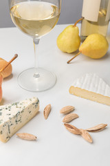 Closeup view of brie and blue cheese with almond, pears, wine glass, bottle and baguette on gray