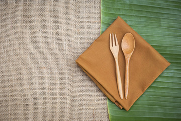 Wooden fork and spoon design on brow napkin over fresh green banana leaf and hessian fabric background