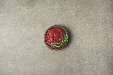 top view of sauce with rosemary twig served in bowl on grey concrete tabletop