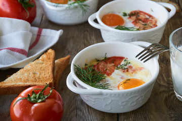 Baked eggs with tomatoes and dill on a wooden table      