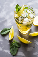 A glass glass with a cold tea with ice, mint and lemon on a gray concrete background. Summer cooling drink