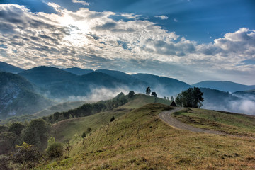 Beautiful mountain landscape of a foggy morning with and old house, trees and clouds, Dumesti, Salciua, Apuseni, Romania