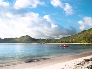 Obraz premium Red motor boat anchored off a sunny Seychelles beach with distant clouds and shoreline