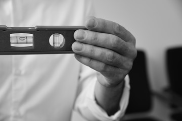 Business man in smart clothes showing building bubble spirit level on camera. Instruments, tools for renovation apartment room. Repair home concept. Black and white