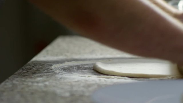 Close up hands of unrecognizable restaurant chef using rolling pin to roll out dough on floured surface, side view