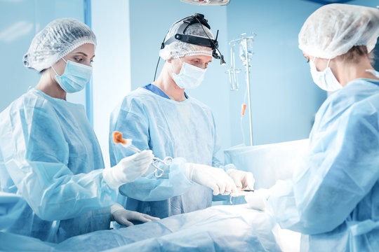 Difficult operation. Professional smart serious surgeons wearing medical uniform and working while performing a difficult operation