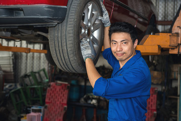Obraz na płótnie Canvas Asian mechanic looking under the car to repair the engine with work board in hand, japanese mechanic portrait style, mechanic maintenance working under car
